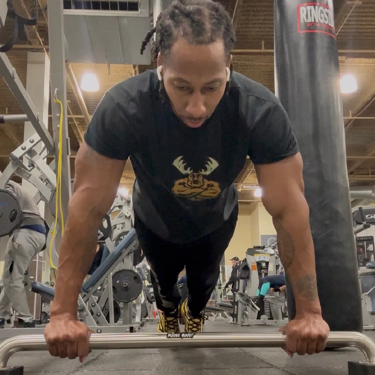 An athlete pressing out a push-up on the Moose Boost Push-Up Bar, hands gripping the branded chrome bar, wearing a Moose Boost antler-mark tee.